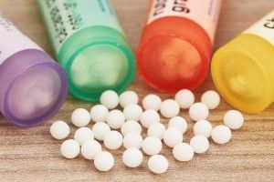 Homeopathic globules scattered around with their colored containers in the shape of tube on a wooden table